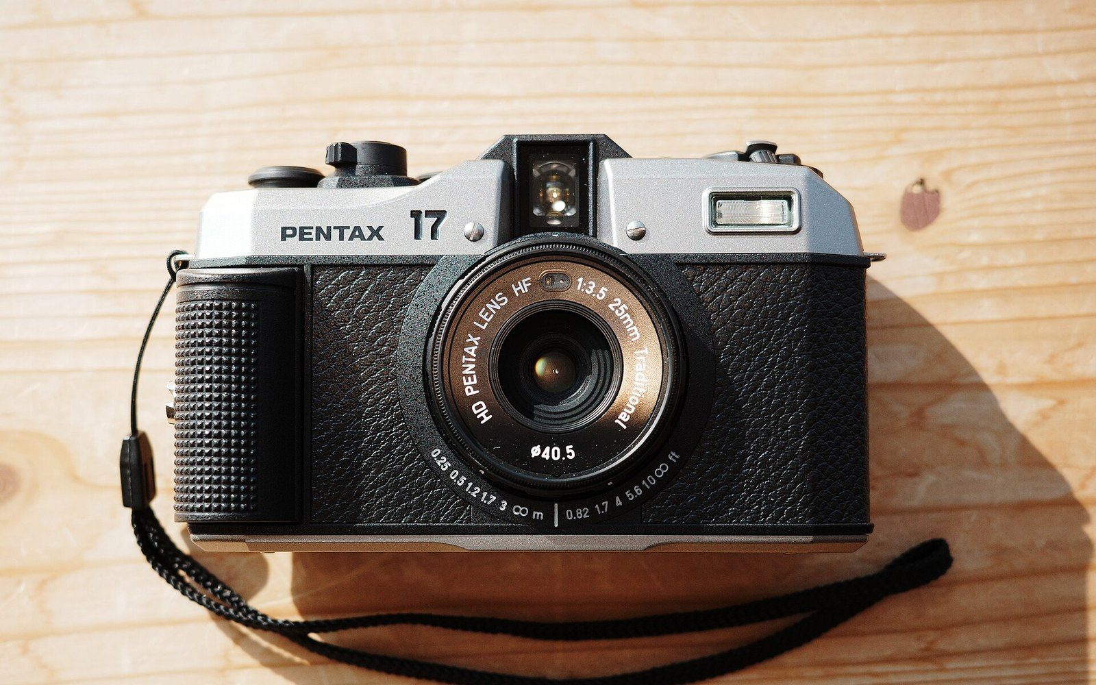 A 35mm film canister, a loaded take-up spool, and a Pentax 17 body on a wooden darkroom counter, a safelight glowing amber in the background