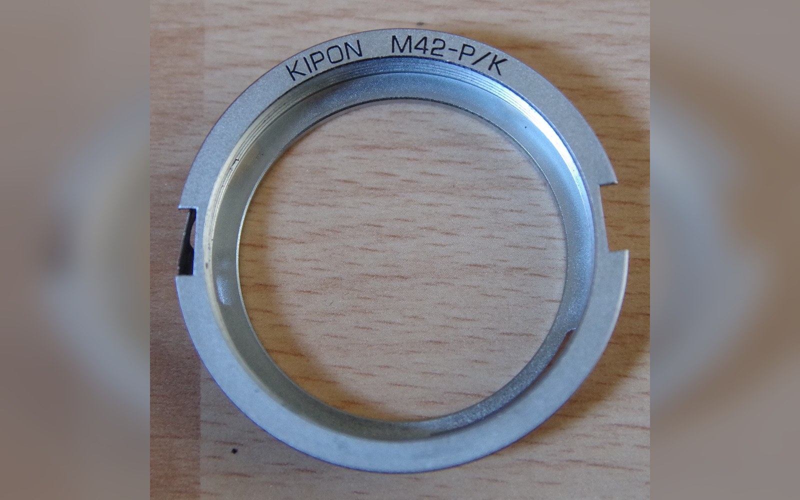 Metal Kipon M42-to-Pentax K lens mount adapter ring on a wooden surface