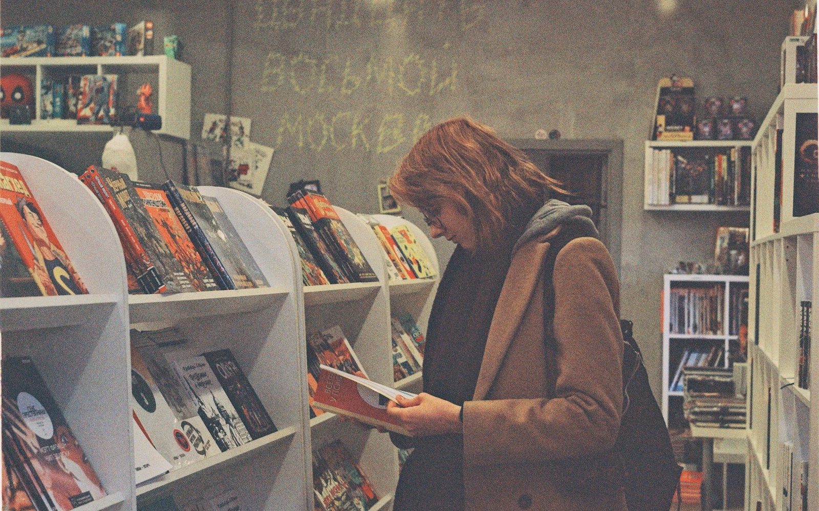 Woman browsing comic books at a shelf in a bookstore with graffiti-covered wall