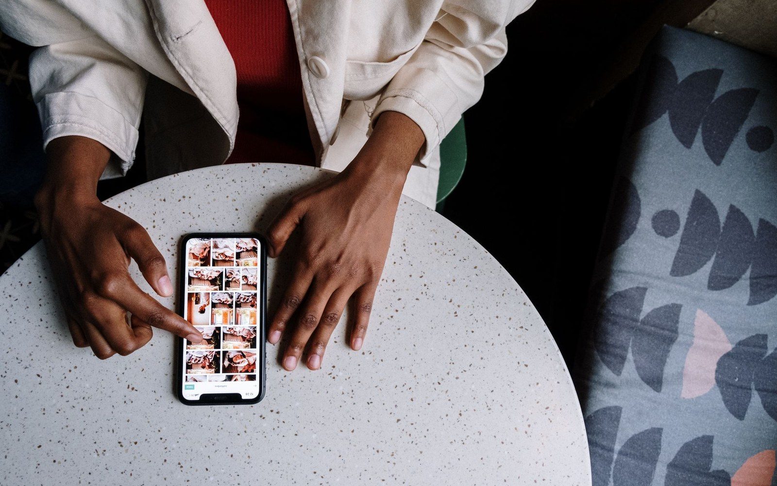 A person scrolls through a photo grid on a smartphone resting on a round table