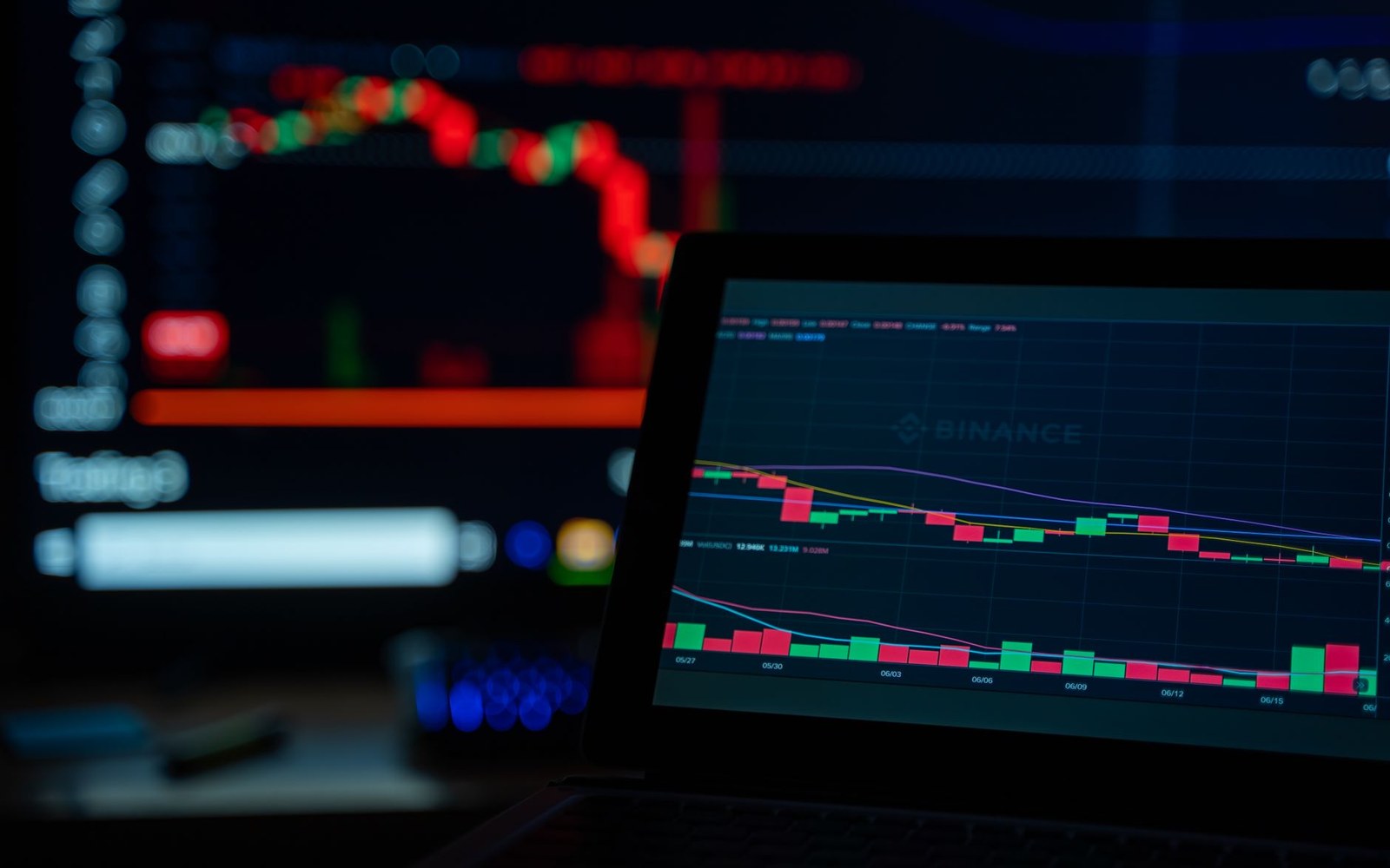 Laptop screen showing a Binance candlestick trading chart with a blurred monitor in the background
