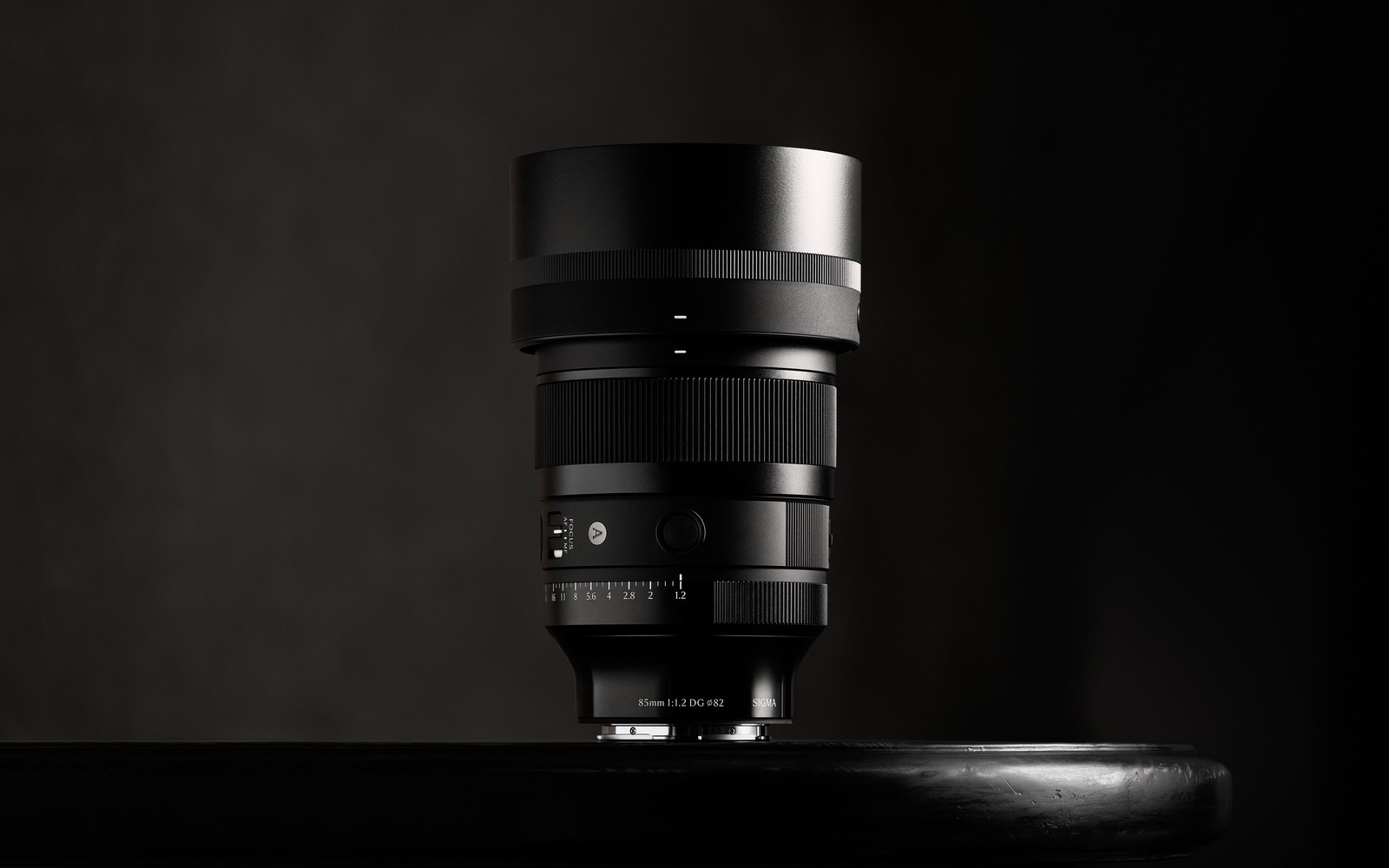 A Sigma 85mm f1.2 DG Art lens standing upright on a dark reflective surface