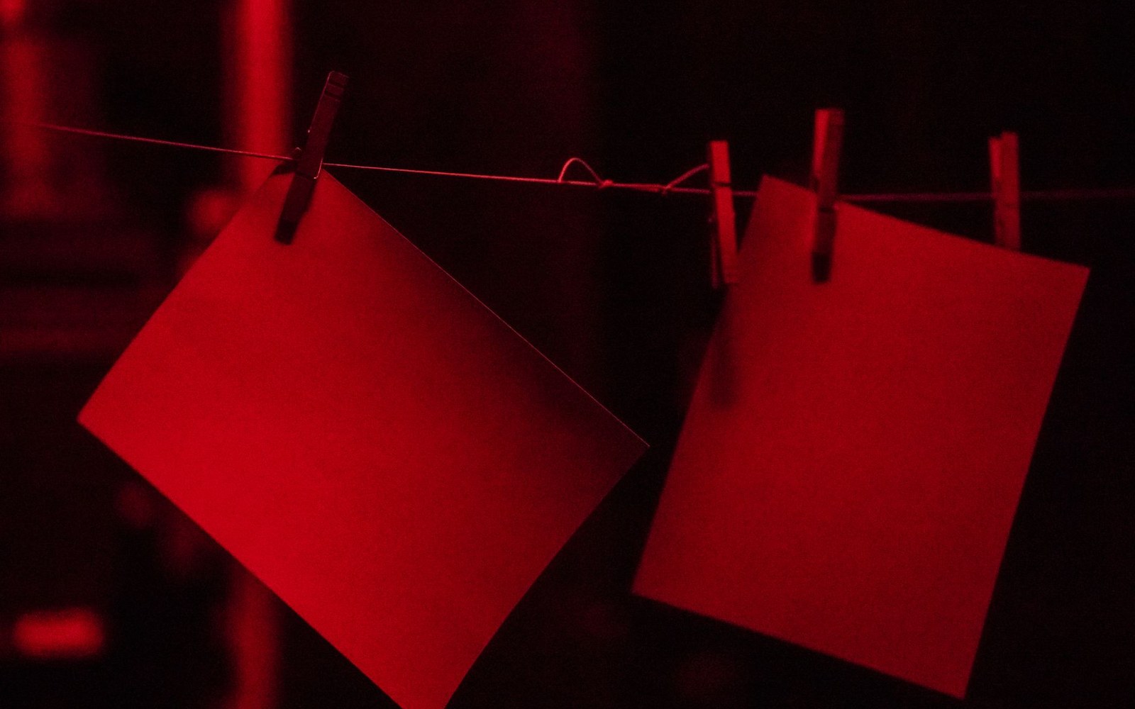 A fibre-based darkroom print hanging to dry on a line, a pair of adult hands adjusting the clip, darkroom shelving visible behind