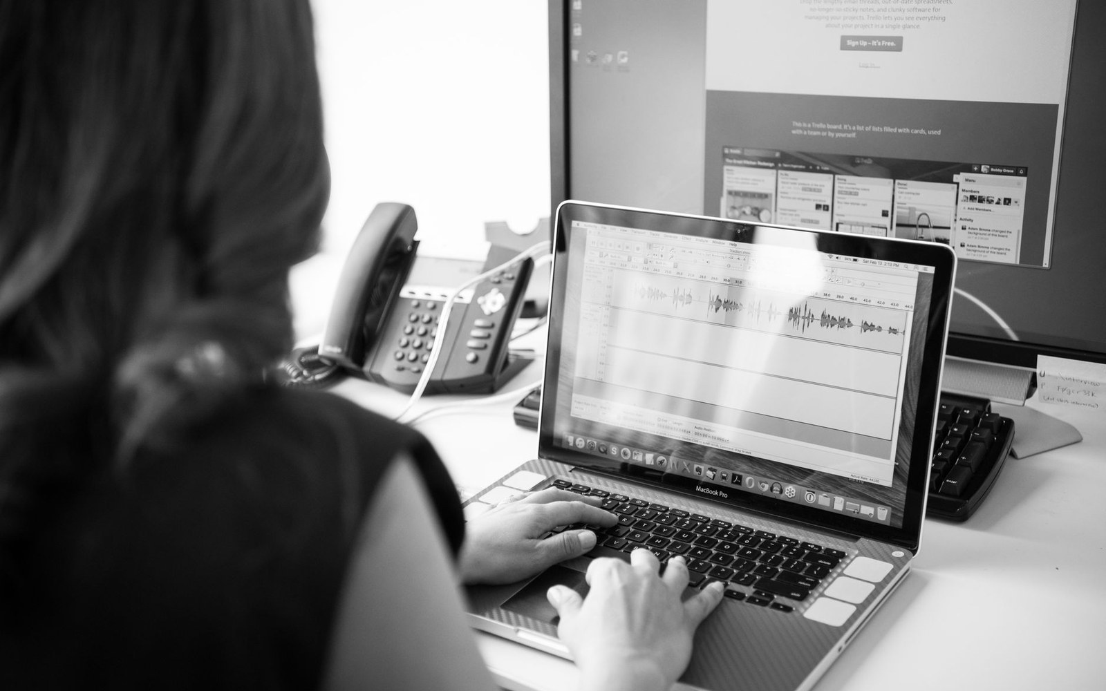 A desktop monitor showing a Capture One raw-processing session with a histogram open and a full-resolution landscape file on the editing canvas, adult hands on the keyboard